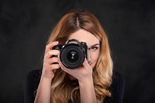 Beautiful young woman with a camera on a dark background.