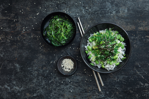 Vegan Rice bowl with avocado, edamame and chuka seaweed salad. Flat lay top-down composition on dark background.