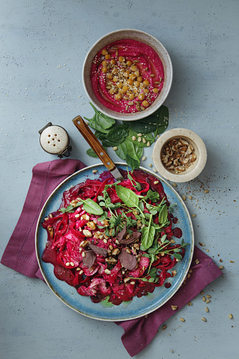 Leftover Turkey pasta with creamy beet sauce, seeds, walnuts, microgreen and beetroot chips. Vegan beetroot hummus. Flat lay top-down composition on blue background.