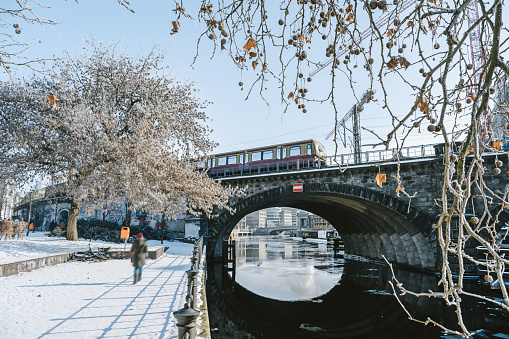 subway train passing historic bridge over snowy park and Spree river in central Berlin on a clear blue winter day