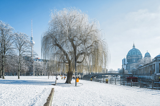 snowy park alongside the river in berlin with cathedral and tv tower in the background on clear sunny winter day