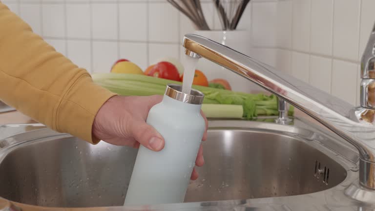 Closed up, slow motion: Man fills up reusable water bottle in the kitchen