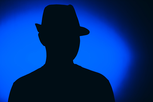 Silhouette of a young man against blue background. He is wearing a hat.