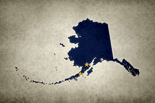 Grunge map of the state of Alaska (USA) with its flag printed within its border on an old paper.