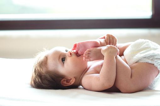 Feet in mouth baby is lying on back in happy baby pose and is looking up