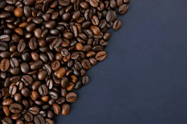 Roasted coffee beans on a dark background. Coffee beans texture. Coffee in beans on dark background. Food background of coffee beans. Abstract background texture. Flat lay. Space for text. Template.