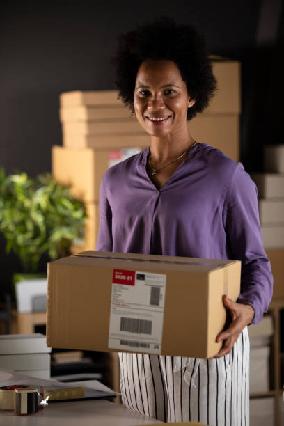 istock Confident female entrepreneur holding a labeled package and smiling at camera 1302474941
