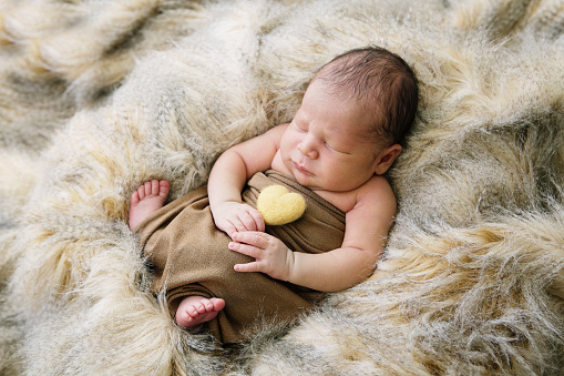A newborn baby sleeps, holding a felted heart.