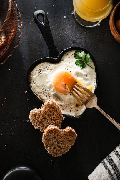flat lay de ensolarado lado até ovo em forma de ovo frigideira de ferro fundido e pão em forma de coração - eggs breakfast heart shape fried egg - fotografias e filmes do acervo
