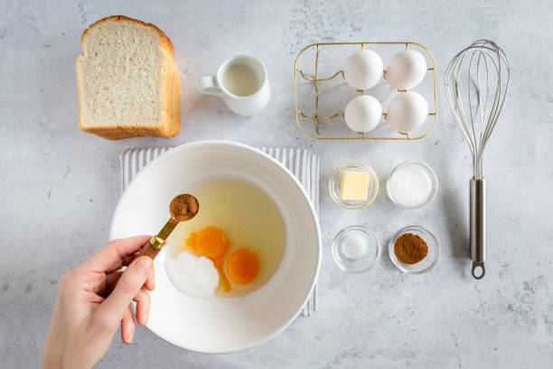 Ingredients for making french toast (or wentelteefjes in Dutch)  on white grey background, woman holding spoon with cinnamon,  view from above Minimal style flat lay of ingredients for making french toast (or wentelteefjes in Dutch)  on white grey background, woman holding spoon with cinnamon,  view from above, food knolling french toast stock pictures, royalty-free photos & images