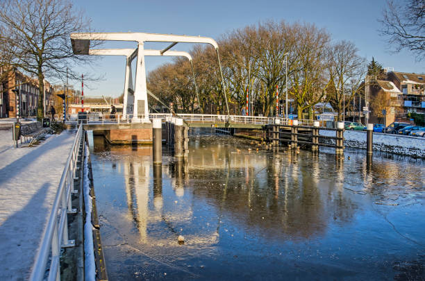 Bridge across a canal in winter Delft, The Netherlands, February 13, 2021: white steel drawbridge reflecting in the flakes and broken ice on Rijn-Schie canal on a sunny day in winter delft winter netherlands snow stock pictures, royalty-free photos & images