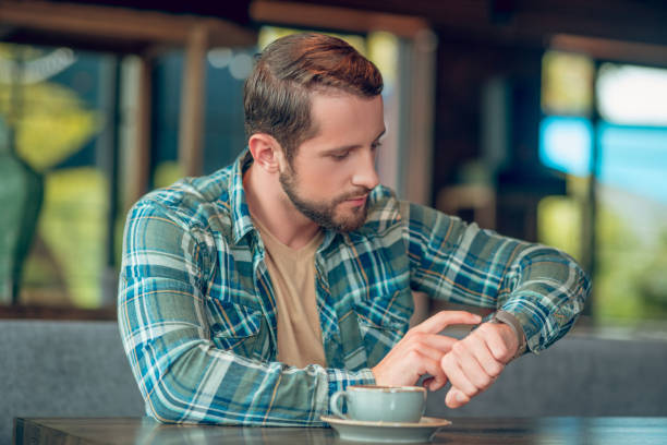 istock Serious man looking at watch sitting in cafe 1302490494