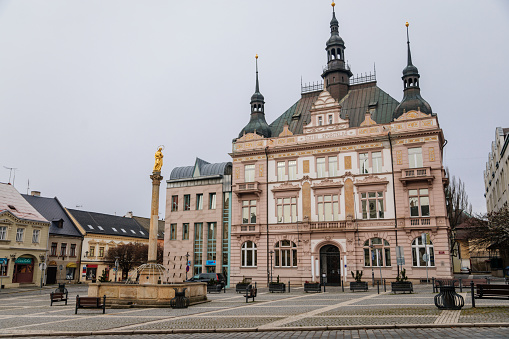 Neo-renaissance house of Ceska sporitelna and Fountain with golden Marian statue, baroque historical buildings, Square of Bohemian Paradise in winter day, Turnov, Czech Republic, January 01, 2021