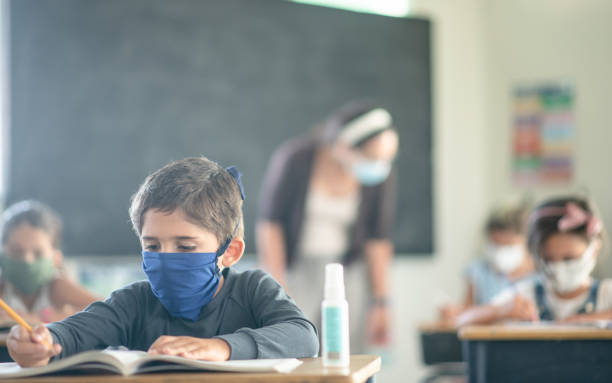 istock School boy wearing a mask in class 1302499110
