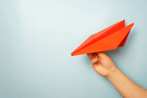 istock A woman's hand holds a red paper airplane on a pale blue background 1302499295
