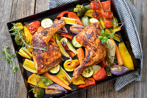 Two crispy oven roasted chicken legs on colorful mediterranean vegetables hot served on the baking sheet