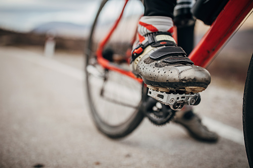 One man, professional male cyclist foot on bicycle pedal on road alone.