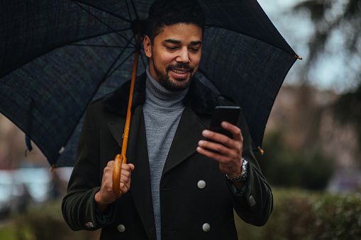 Young businessman using smart phone under umbrella