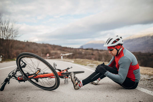 ciclista masculino cayó de su bicicleta en la carretera - on one knee fotografías e imágenes de stock