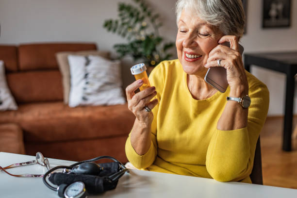 Senior woman talking with a doctor on the phone and holding a pill bottle Photo of senior woman at home preparing to drink medical pill. She is holding a pill bottle and talking on the phone with a doctor old woman smiling tablet stock pictures, royalty-free photos & images