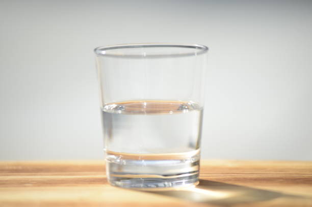 istock Half full or half empty glass of water on wooden surface with bright blurred out background, centered 1302517095