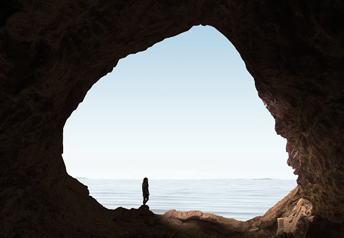 Woman looking out of cave at sea