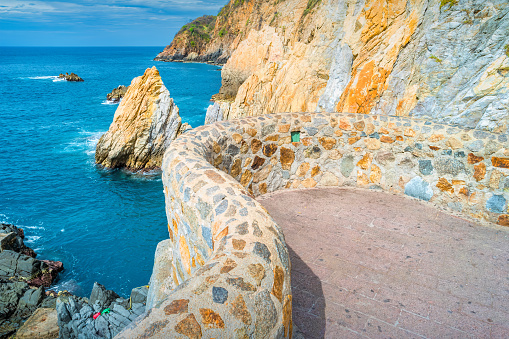 Photo of the landmark La Quebrada diving cliffs and waterfront promenade in Acapulco, Mexico. La Quebrada is famous for the divers that entertain tourists by jumping off the cliff.