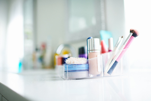 Make-up products and brushes in plastic container in modern bright bathroom
