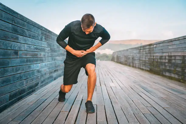 Photo of Man runner having stomach side cramps or stitch during training. Athlete suffering from pain in his side. Side pain after jogging or running.