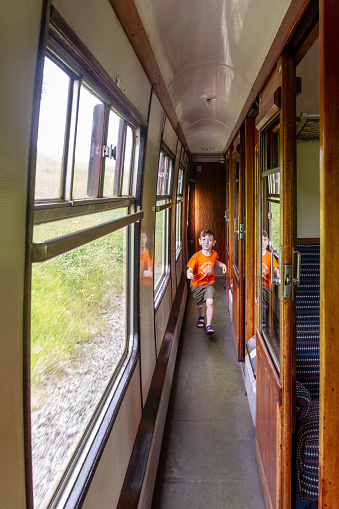 A cute, blue-eyed, red-haired, 4 years old boy running towards camera on a vintage steam train corridor