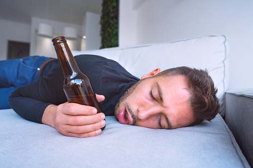 Joven borracho con la boca abierta y botella de cerveza durmiendo en el sofá de casa. photo