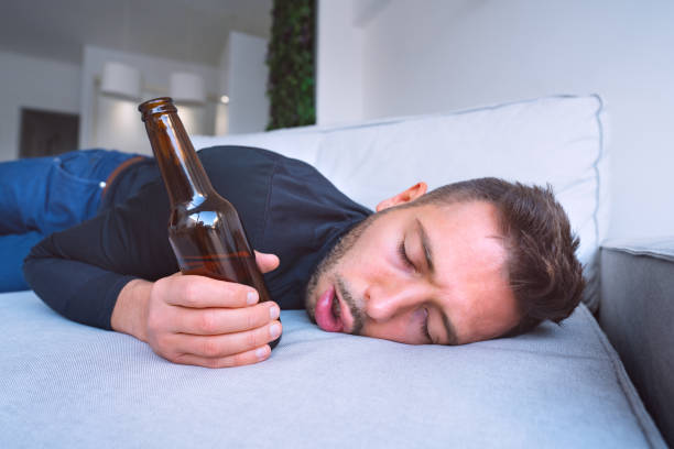 drunk young man with open mouth and bottle of beer sleeping on the sofa at home. - ressaca imagens e fotografias de stock