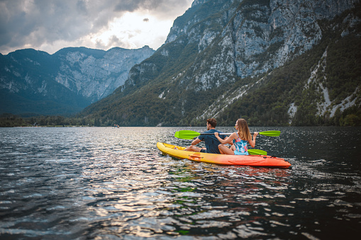 Mid adult couple enjoying active lifestyle on weekend as they paddle kayak across lake in Triglav National Park with Julian Alps in background.
