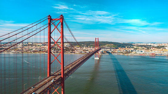 Aerial view or drone photo of the 25 De Abril Bridge. Red Lisbon bridge is connecting Lisbon city and Almada across the Tajo river. Portugal sightseeing. High quality photo