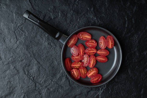 istock Half cut fresh cherry tomatoes on black frying pan on black background 1302538585