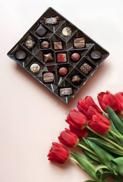 Box of chocolates and red tulips on light pink background. Flat lay, top view.