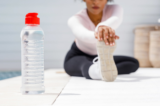 Black Woman In Active Wear Exercising And Stretching With Water Bottle Nearby