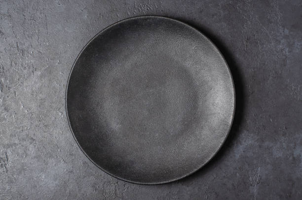istock Dark grey textured concrete background for design with black food plate. Copy space 1302559433