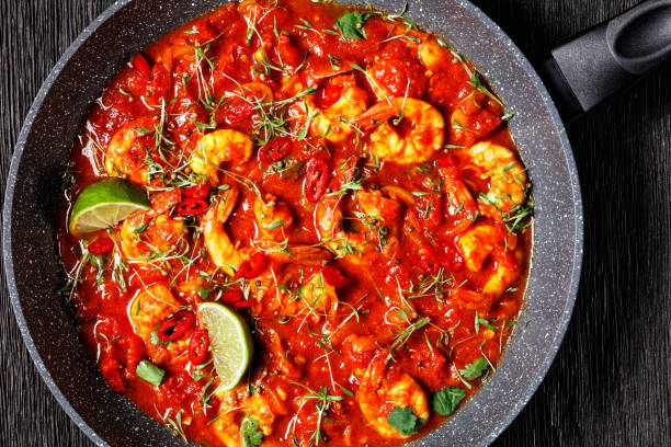 istock Prawn karahi - pakistani tomato shrimp curry with lime juice red chili and red curry paste served on a frying pan with fresh cilantro on a dark wooden background with linen towel, top view, close-up 1302564912