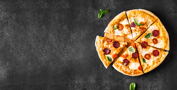 Delicious pizza on black concrete background, top view, copy space. Hot pepperoni, mozzarella cheese and tomatoes pizza with basil.