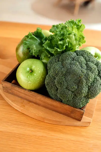 Photo of set of green detox foods: apple, broccoli, lettuce and avocado in a wooden eco-friendly storage box. healthy diet food, vertical food content, selective focus