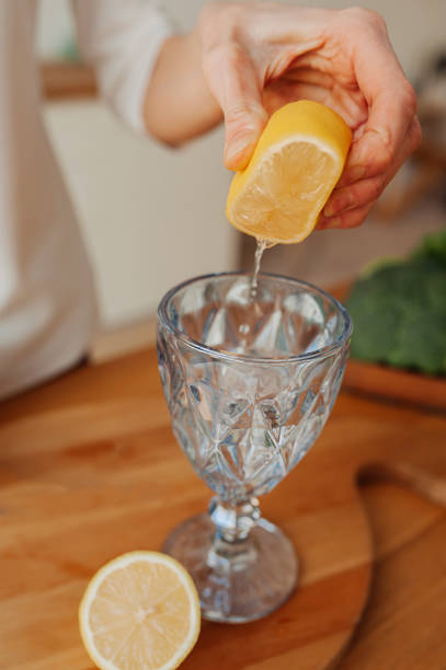istock step-by-step instructions for preparing lemon water. Step 4. woman with no face squeezes the juice from lemon into glass in light kitchen. vertical wellness content, selective focus 1302566096