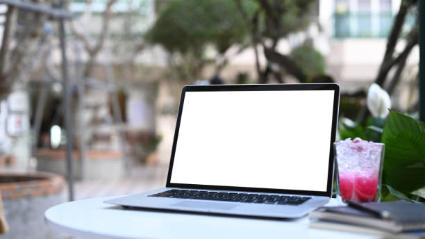 istock Mock up computer laptop with blank screen, notebook and fresh drink on white desk in cafe. 1302567079