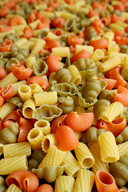 istock Vertical image of heap of three-color uncooked vegeroni pasta with selective focus 1302570455