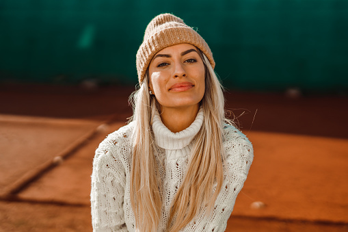 Portrait of a beautiful young woman with long blond hair wearing an apricot color knit beanie hat outdoors in the city