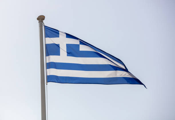 istock Greek flag on flagpole waving on blue sky background 1302572197