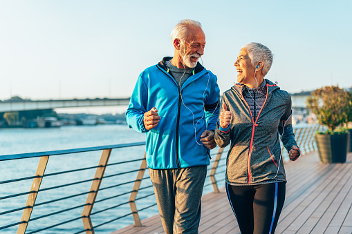 Senior couple in sports clothing and sports technologies jogging together across the bridge