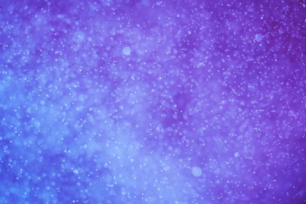 abstrakter festlicher hintergrund mit selektivem fokus. helle partikel auf dunkelblauem hintergrund. spritzer, raum, energiefluss - purple backgrounds illuminated defocused stock-grafiken, -clipart, -cartoons und -symbole