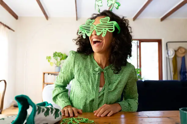 Caucasian woman dressed in green with shamrock glasses for st patrick's day laughing. Staying at home in self isolation during quarantine lockdown.