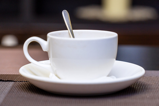 An empty white coffee cup with a teaspoon on the table. Selective Focus